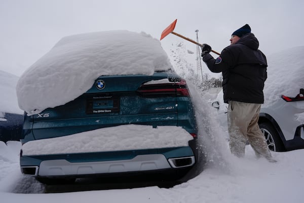 Cary Fallath, the BMW Store lot technician, clears snow from new cars in Silverton, Ohio, Tuesday, Jan. 7, 2025. (AP Photo/Carolyn Kaster)