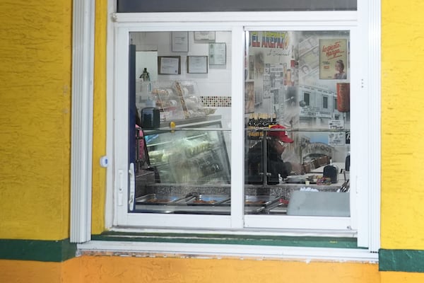 A patron of Venezuelan restaurant El Arepazo is seen through a window as Venezuelan community leaders gather outside for a press conference to denounce changes to the protections that shielded hundreds of thousands of Venezuelans from deportation, Monday, Feb. 3, 2025, in Doral, Fla. (AP Photo/Rebecca Blackwell)