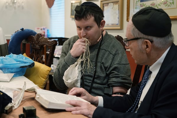 Dov Marcus, left, kisses the knotted fringes -- known as tzitzit – of his prayer shawl after wrapping the leather straps of tefillin and praying with his uncle, Chaim Orlan, in Teaneck, N.J., on Friday, Dec. 20, 2024. (AP Photo/Luis Andres Henao)